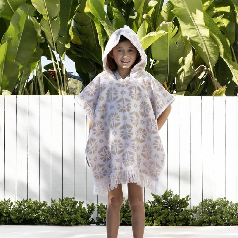 alt="A kid wearing a natural poncho featuring a stylish floral pattern with knotted tassels along the ends"