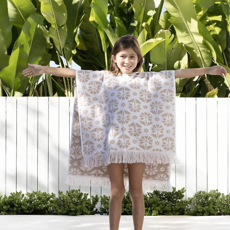 alt="A kid wearing a natural poncho featuring a stylish floral pattern with knotted tassels along the ends"