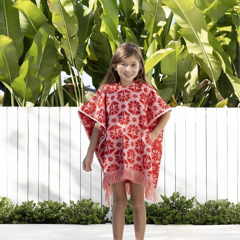 alt="A kid wearing a red poncho featuring a stylish floral pattern with knotted tassels along the ends"