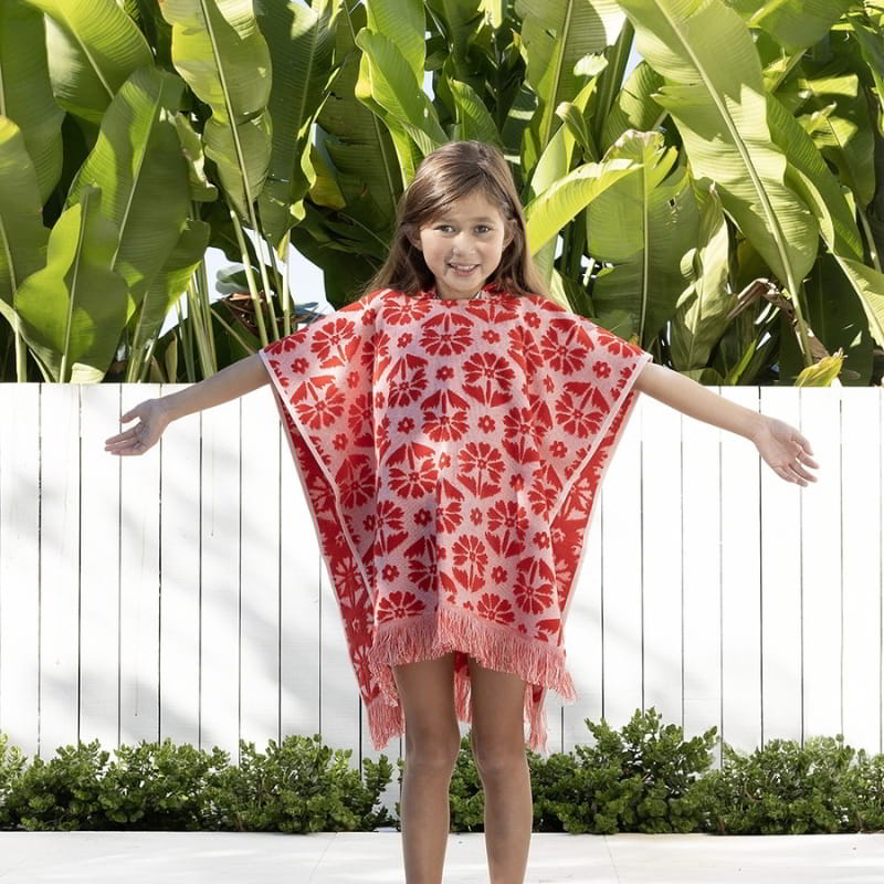 alt="A kid wearing a red poncho featuring a stylish floral pattern with knotted tassels along the ends"