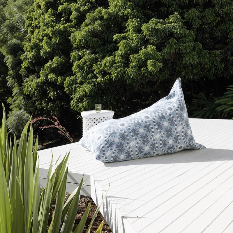 alt="A light blue and dark blue designed with palm tree pattern bean bag in an outdoor setting"