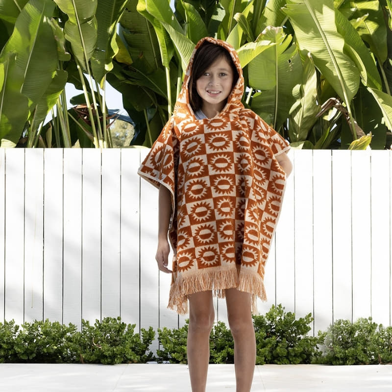 alt="A kid wearing a brown poncho featuring a stylish sun pattern with knotted tassels along the ends"