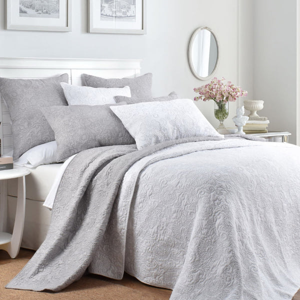 alt="A cotton coverlet set designed with a floral embossed pattern in white and subtle greys in a cosy bedroom"