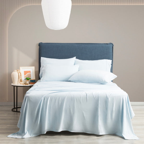 Luxurious bed with crisp blue sheet sets and plump pillows, elegantly placed against a tastefully adorned wall.