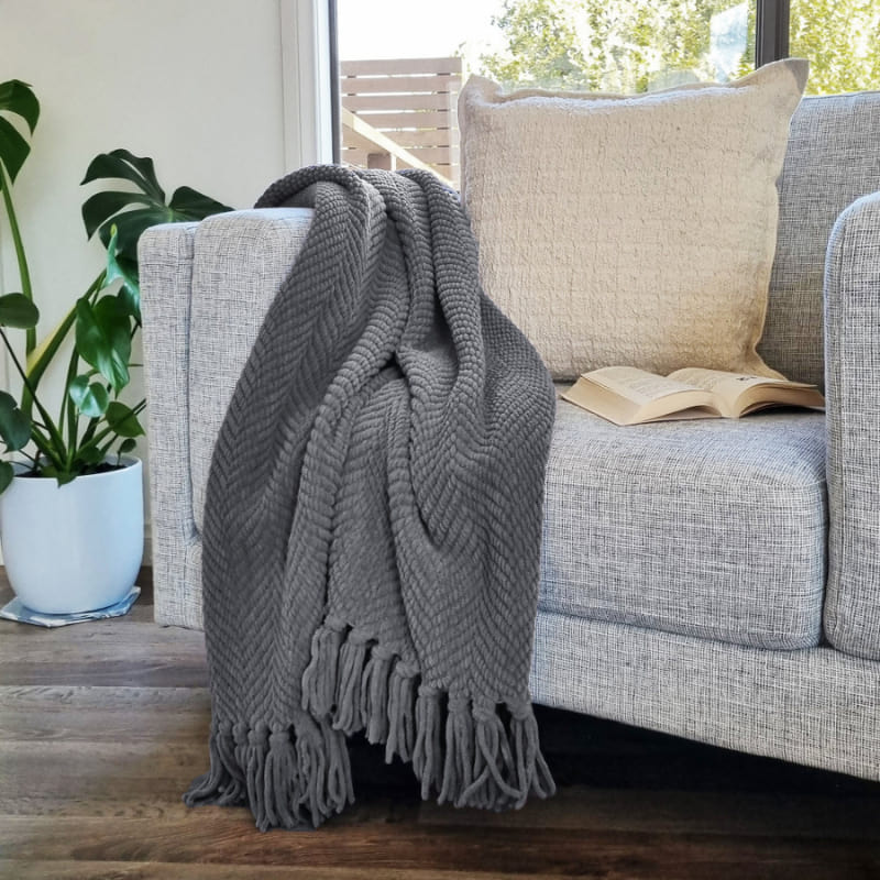 A stunning grey throw in on couch with pillows, boasting chevron weave and knotted fringe. 