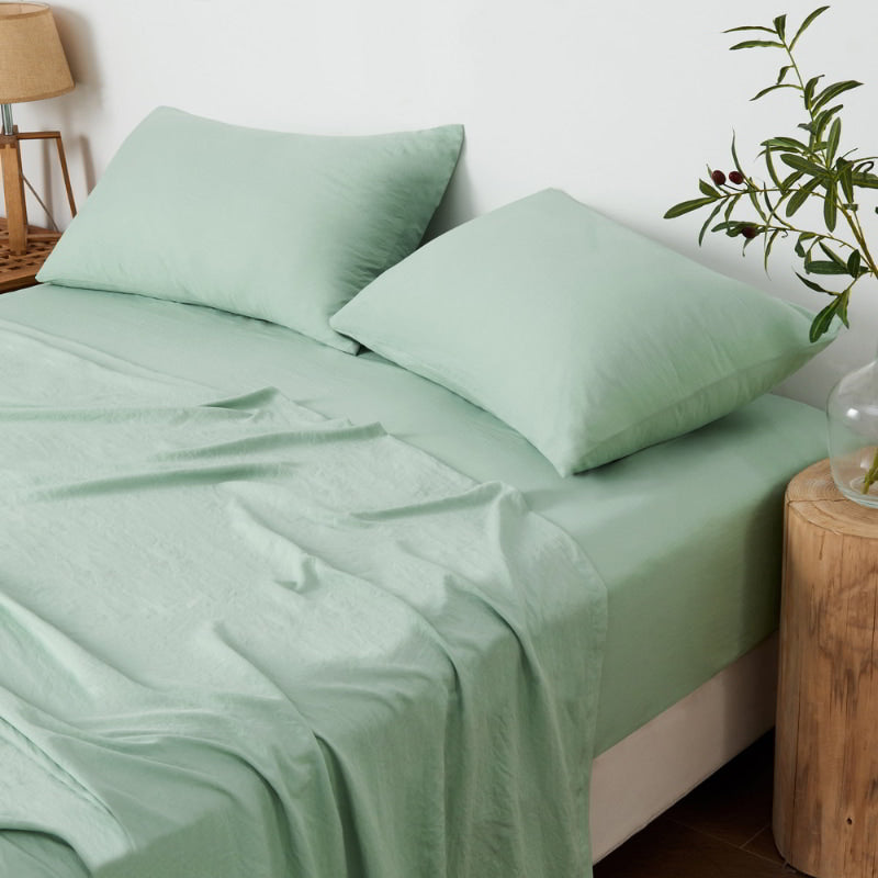 alt="A luxuriously soft sage cotton pre-washed sheet set in a cosy bedroom"