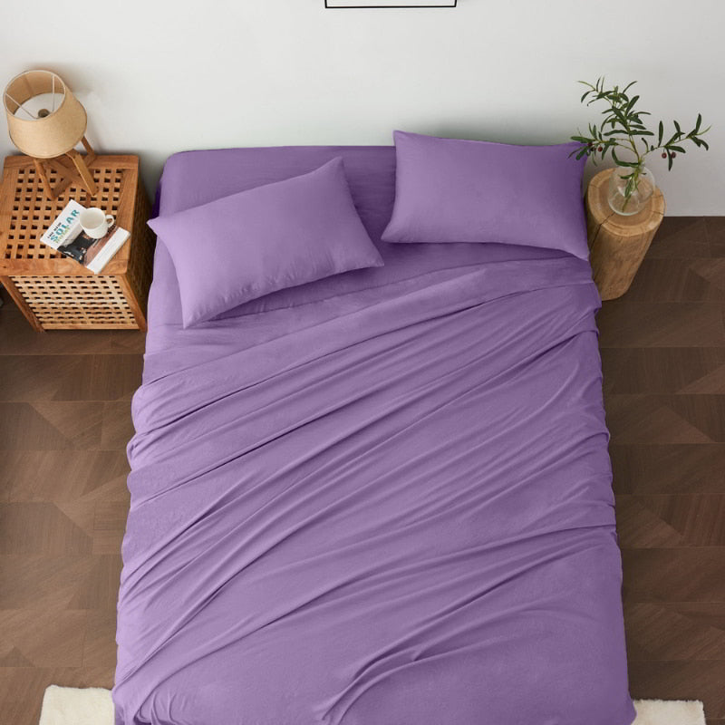 alt="A luxuriously soft lilac cotton pre-washed sheet set in a cosy bedroom"