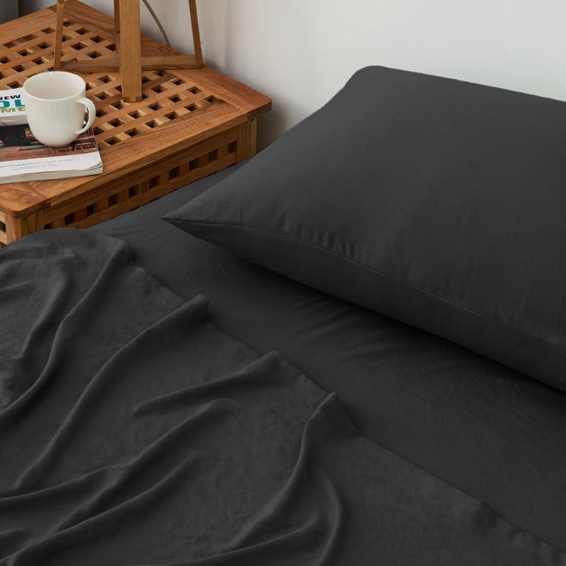 alt="A luxuriously soft black cotton pre-washed sheet set in a cosy bedroom"