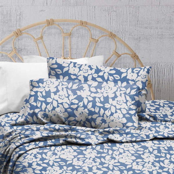 A blue bed sheets and pillows, adorned with a monochromatic white floral and foliage pattern, craft a serene and unique design.