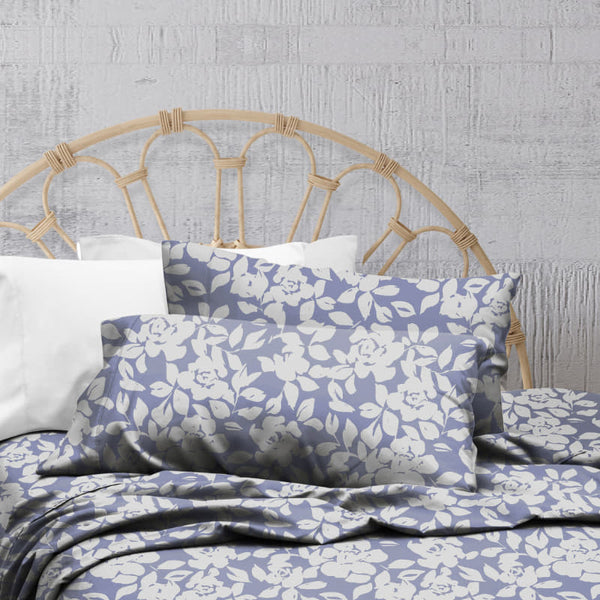 A lavender-toned bed sheets and pillows, adorned with a monochromatic white floral and foliage pattern, craft a serene and unique design.