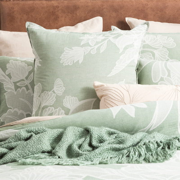 A sumptuous bed, embellished with soft pillows and a sage green blanket, accompanied by a european pillowcase adorned with a charming floral design.