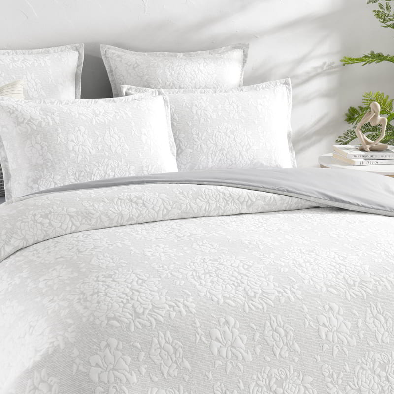 alt="Showcasing an ivory quilt cover set infused with blooming flower bundles in a luxurious bedroom"