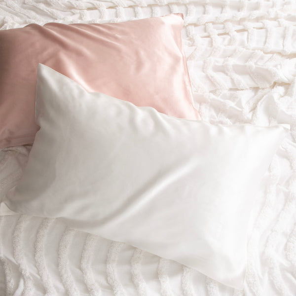 alt="Pink and white pillowcase on a white bed. Crafted from 100% pure mulberry silk, these luxurious pillows offer a refreshing experience for your skin. "