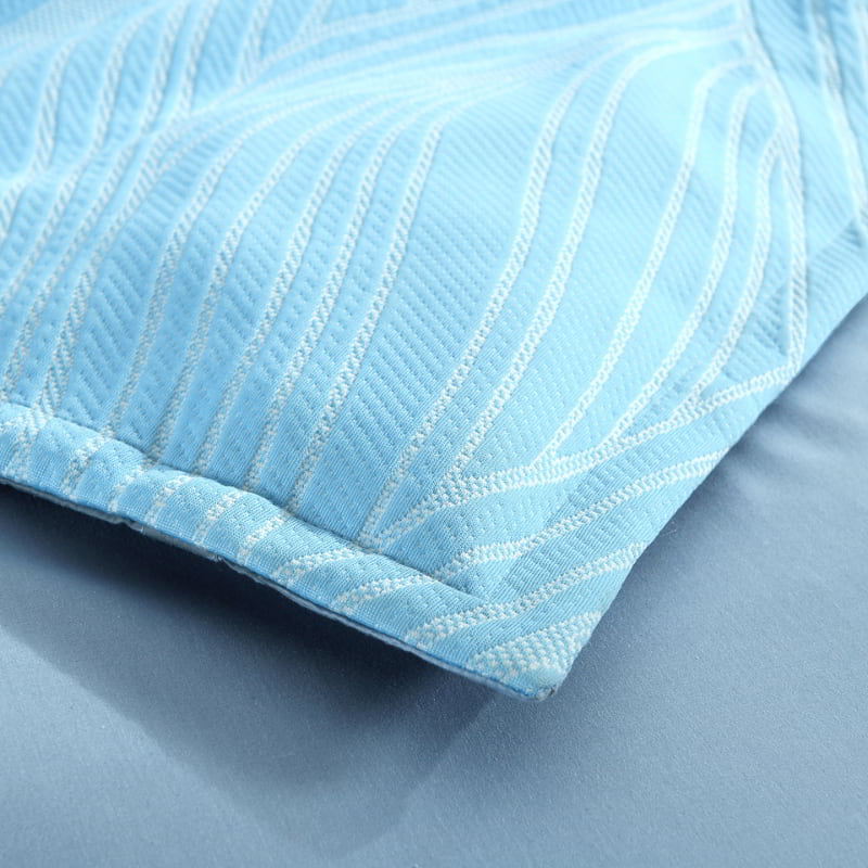 alt="Zoom in details of a shades of blue quilt cover with a beach wave design."