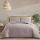 Bed with pink textured bedding in a room with a wicker headboard and hanging light fixture.
