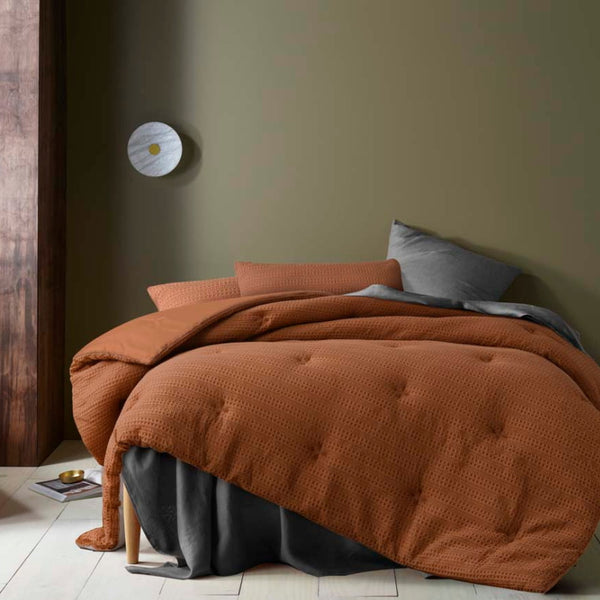 alt="A brown comforter set featuring a detailed geometric design created using a three-dimensional weaving technique"