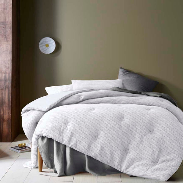 alt="A white comforter set featuring a detailed geometric design created using a three-dimensional weaving technique"