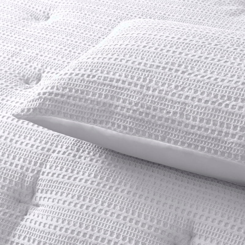 alt="Zoom in details of a white comforter set featuring a detailed geometric design created using a three-dimensional weaving technique along with the pillowcases"