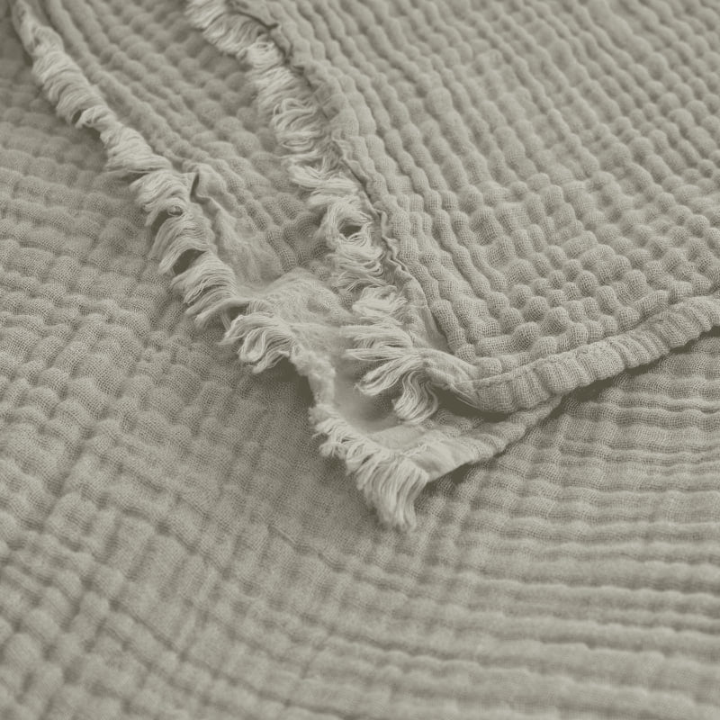 alt="Close-up details of a natural throw featuring a 4 layer gauze cotton fabric with natural frayed edge"