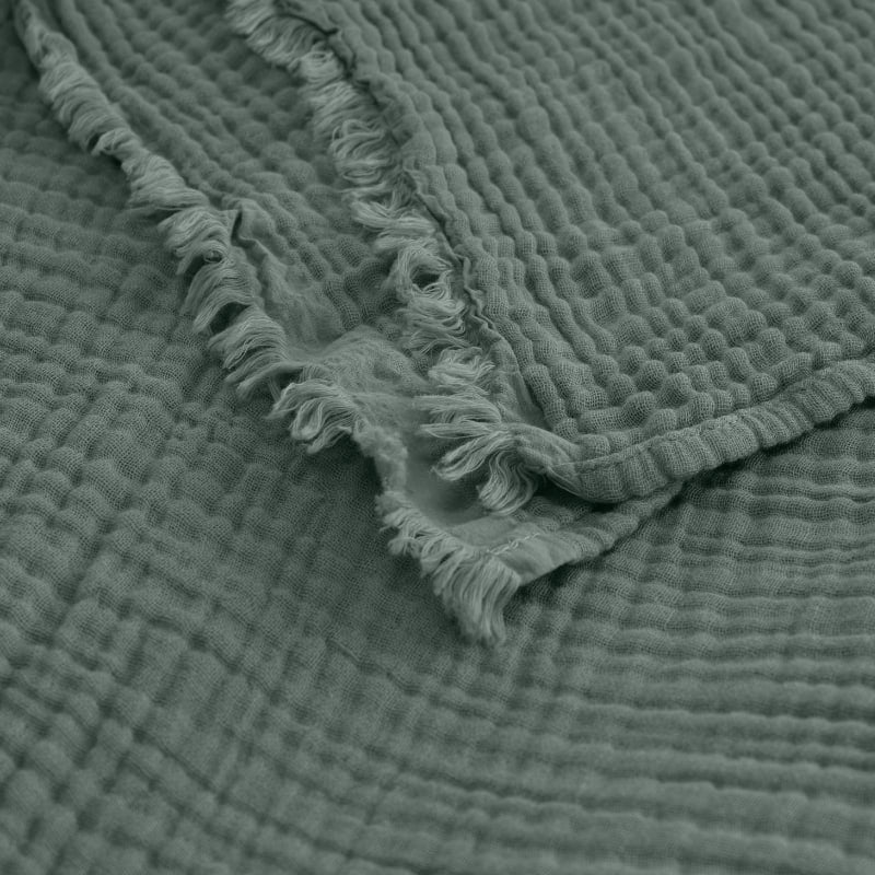 alt="A green throw featuring a 4 layer gauze cotton fabric with natural frayed edge"