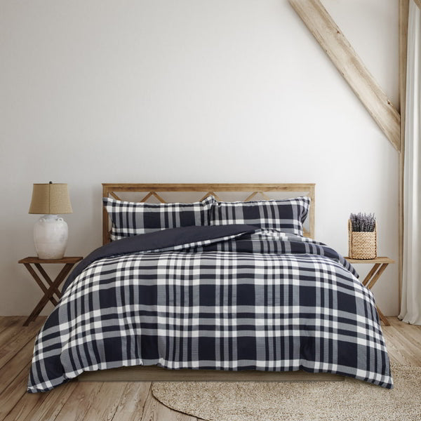 A cosy bed adorned with a navy and white plaid comforter, enhancing the room's classic charm and inviting relaxation.