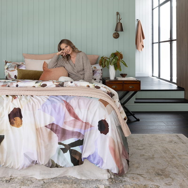 A woman sitting on a bed with a stunning quilt cover set designed with a watercolour flowers in earthy and pastel tones.