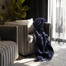 Bambury Asha Navy Throw draped over an armchair in a softly lit living space