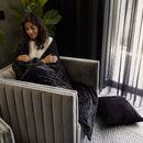 Woman wrapped in the Channel Charcoal Throw, sitting comfortably in a modern chair

