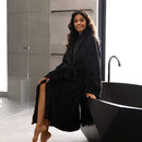A woman wearing an elegant charcoal velvet robe relaxes on the edge of a luxurious bathtub, exuding tranquility and sophistication