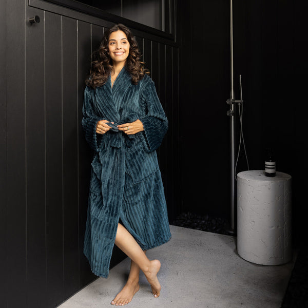 A woman draped in a sumptuous blue velvet robe stands in front of a bold black wall, radiating elegance and refinement.