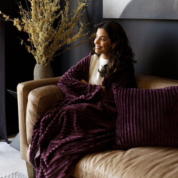 Woman wrapped in the Channel Plum Throw, sitting comfortably in a modern sofa
