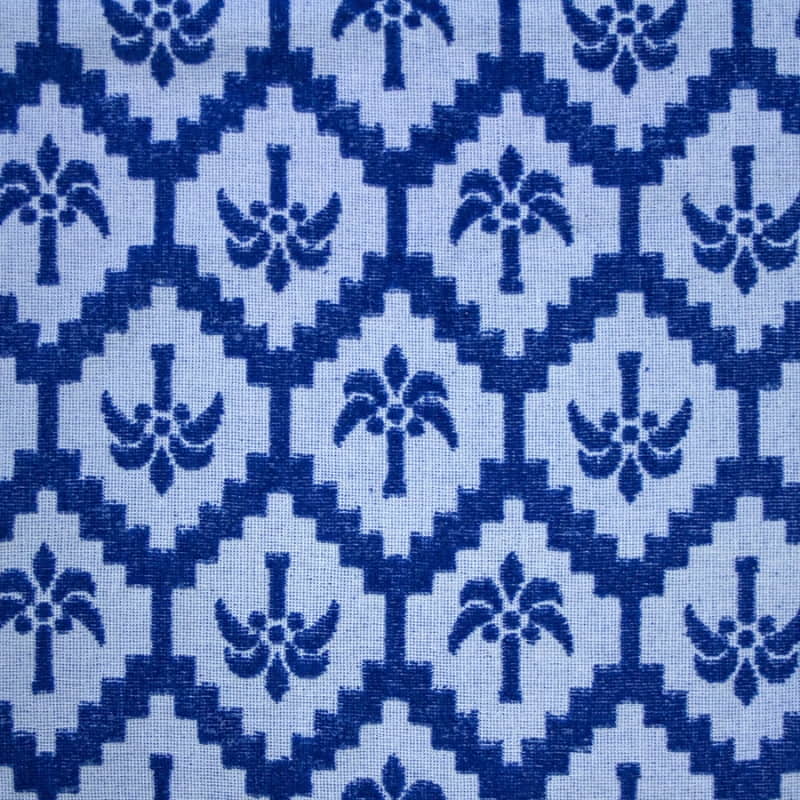 alt="Close-up view of a cobalt blue beach towel designed with palm tree pattern and tassels on both ends"