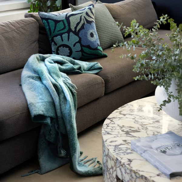 Bambury Cosmo Aqua Throw draped casually over a dark sofa in a styled living space

