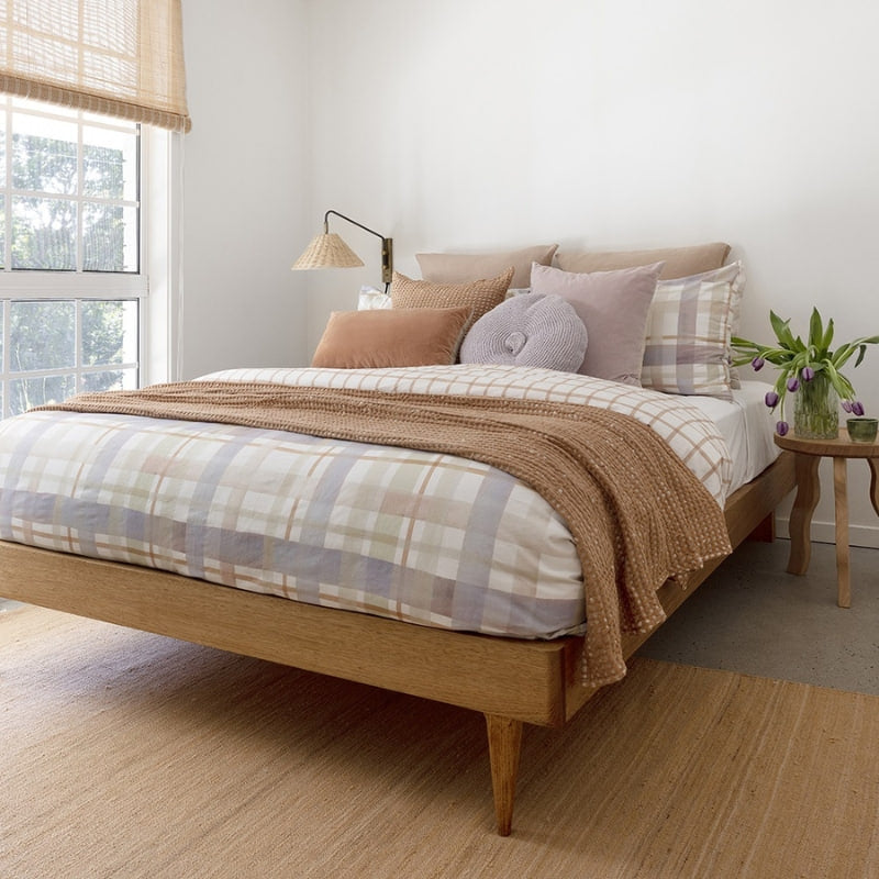 alt="A digitally printed hand-painted watercolour check pattern in sage green, lilac ash, and tan on a crisp white base quilt cover set in a cosy bedroom"