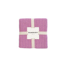 A chic Dora Orchid Throw packaging with a label, designed with two-toned waffle fabric, perfect for enhancing any living space.