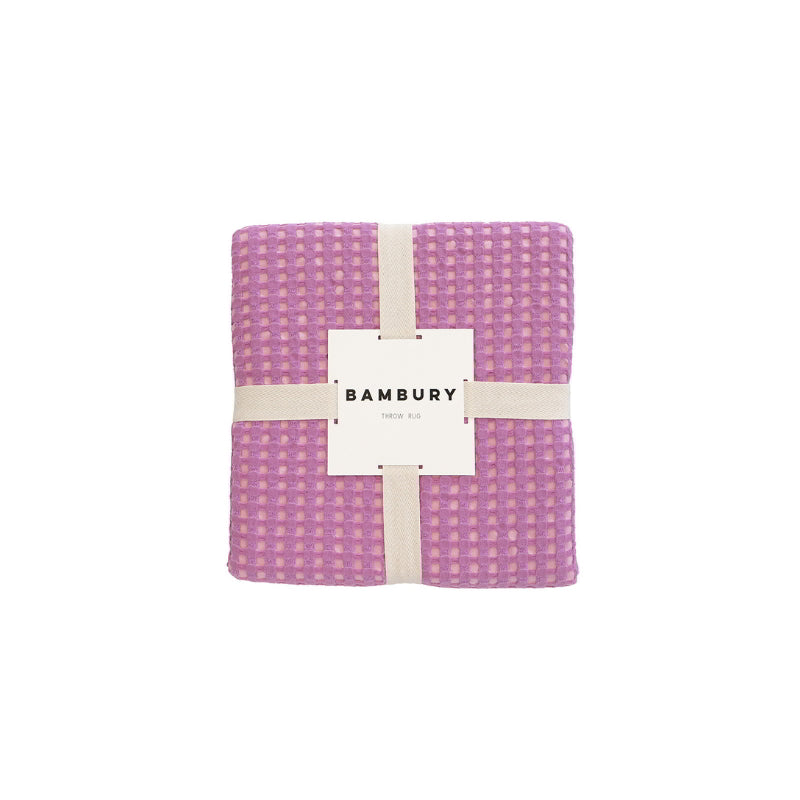 A chic Dora Orchid Throw packaging with a label, designed with two-toned waffle fabric, perfect for enhancing any living space.