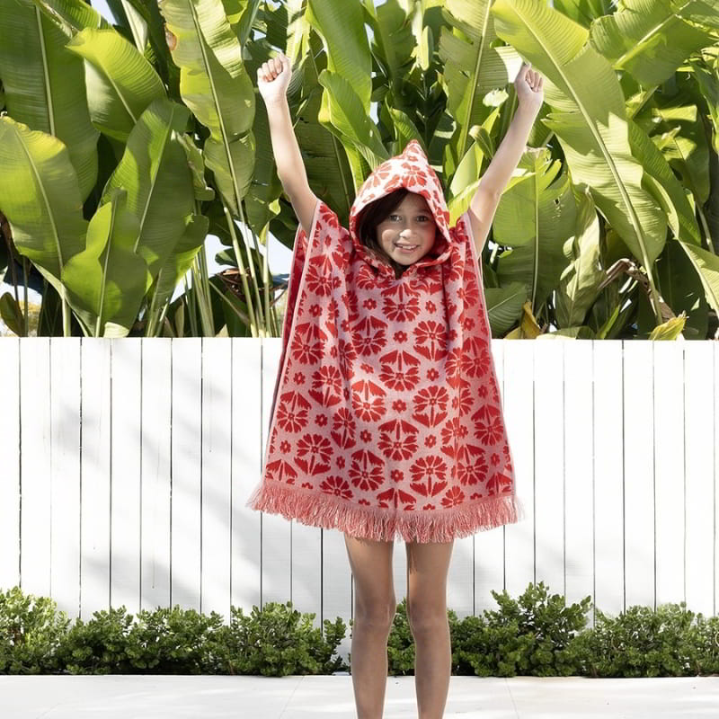 alt="A kid wearing a red poncho featuring a stylish floral pattern with knotted tassels along the ends"