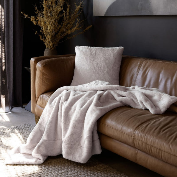 Bambury Frida Snow Throw styled on a tan leather lounge with matching cushion

