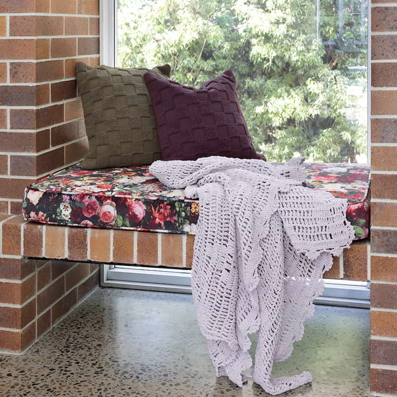 A cosy bench with a blanket and pillow featuring the Harris cushion, a stylish and textured home accent with a checkerboard pattern.