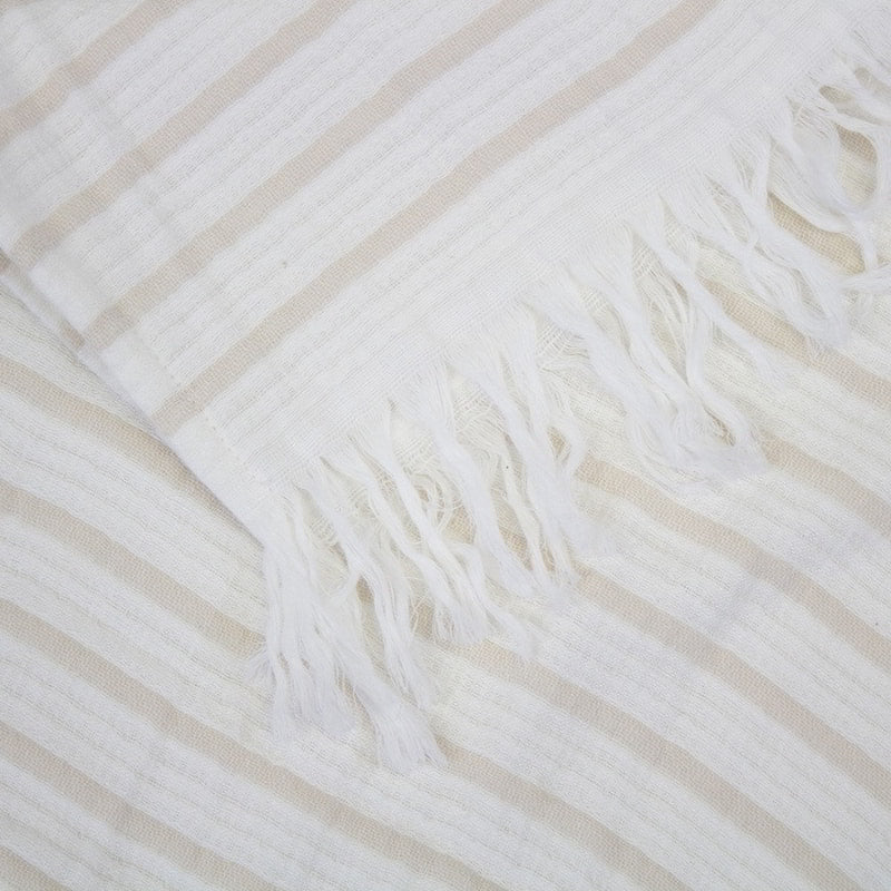 alt="Close-up view of a striped white and natural throw with fringe at both ends"