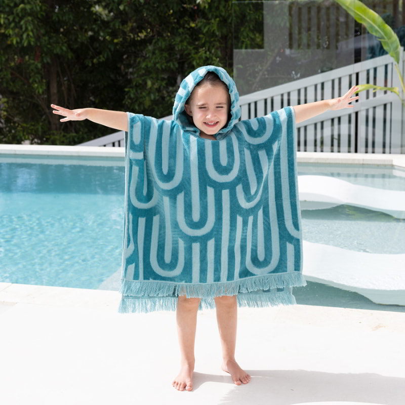 A kid standing beside the pool featuring HiLo blue poncho for kids, ideal for beach or pool use, showcasing a whimsical design and cosy texture.