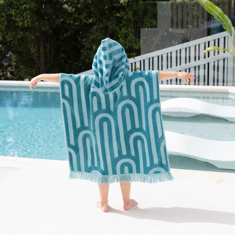 A kid wrapped in a blue and white towel, showcasing the colourful and cosy Bambury HiLo Arcade Kids Poncho.