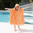 A kid wearing an orange poncho smiles by the pool, enjoying warmth and comfort after swimming.