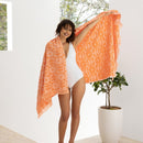A woman in a white bathing suit featuring the HiLo Bloom Peach beach towel with floral design, perfect for drying off or lounging by the pool.