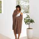A woman cosily standing complemented by a beautiful floral beach towel, perfect for outdoor relaxation.