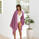 A woman standing showcasing the vibrant pink beach towel featuring a floral pattern perfect for beach days.