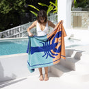 A woman holds a vibrant lobster-patterned beach towel, showcasing its soft velour finish and premium cotton for ultimate comfort.