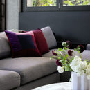 Bambury Jax Berry cushion styled on a grey sofa with rich berry tone