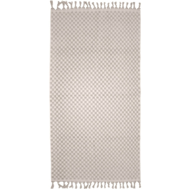alt="A stylish natural beach towel with a small check pattern achieved through a series of high and low sections of towelling finished with a beautiful fringe along the ends"