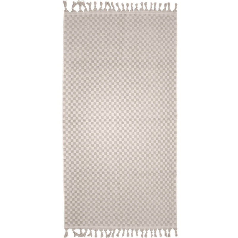 alt="A stylish natural beach towel with a small check pattern achieved through a series of high and low sections of towelling finished with a beautiful fringe along the ends"